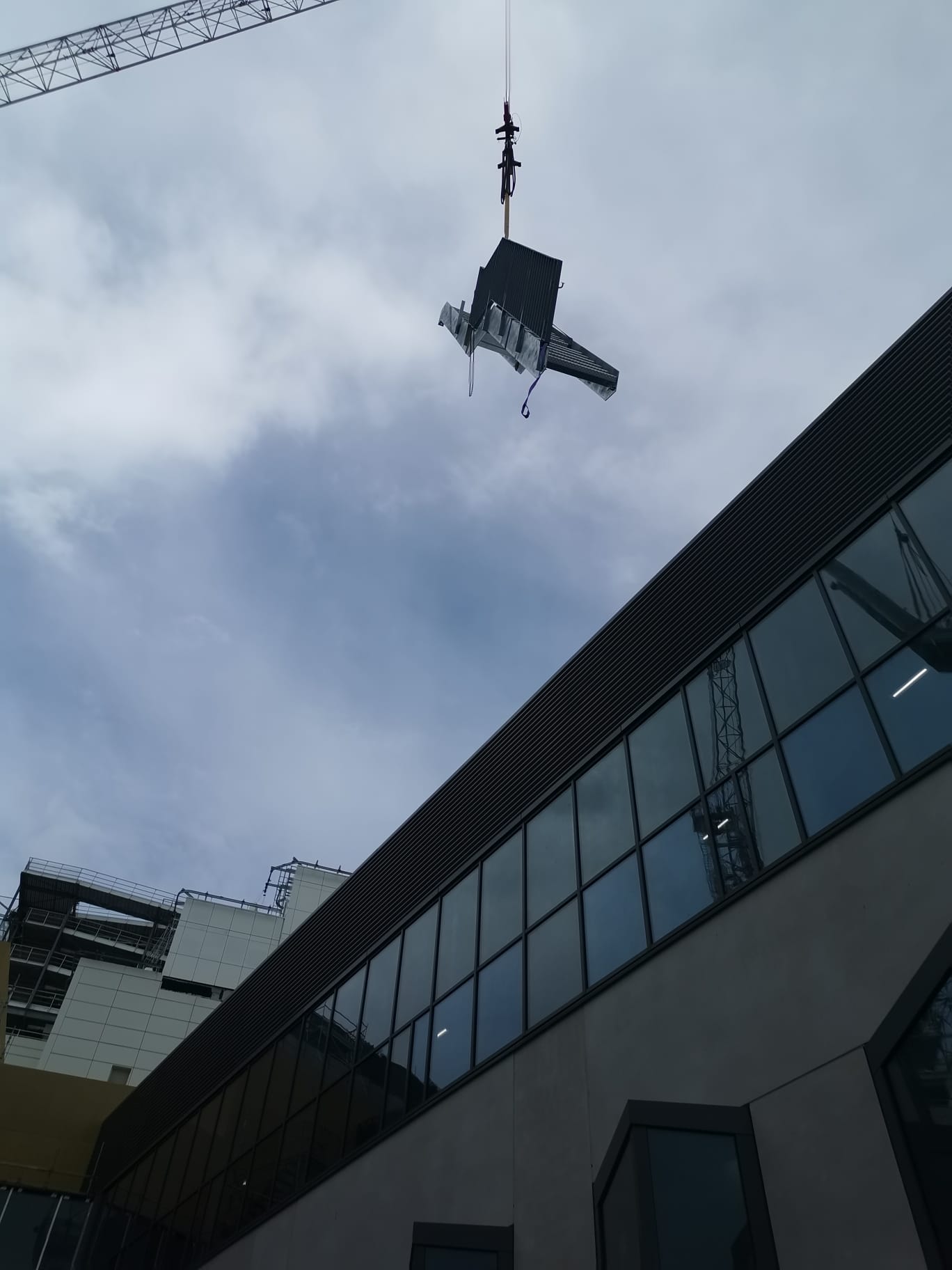 Tower crane lifting a fabricated steel unit above a commercial building