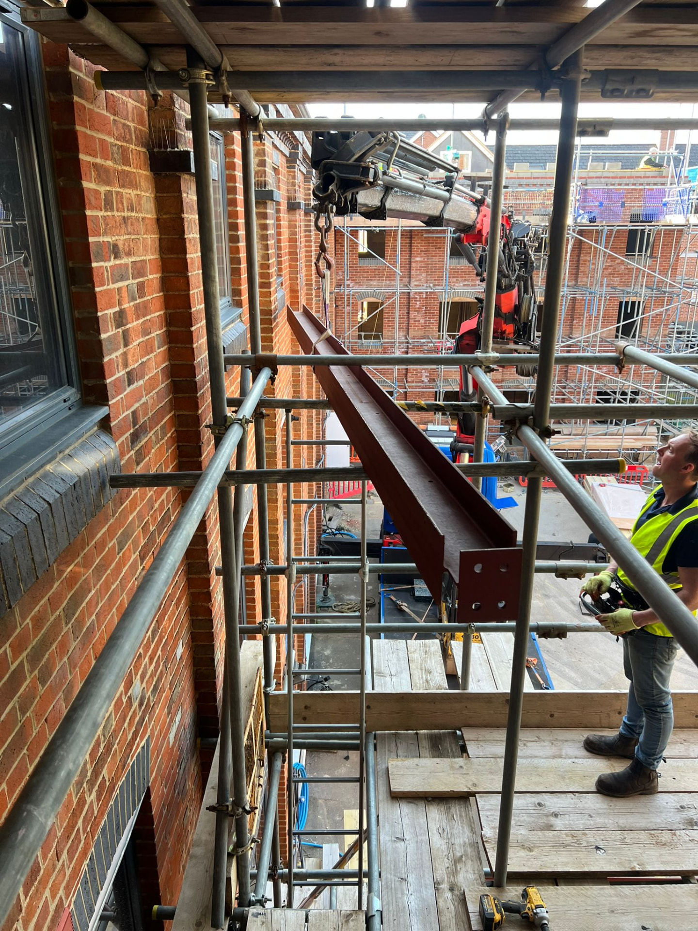 Steel erector guiding a beam lifted by a crane on a scaffolded site