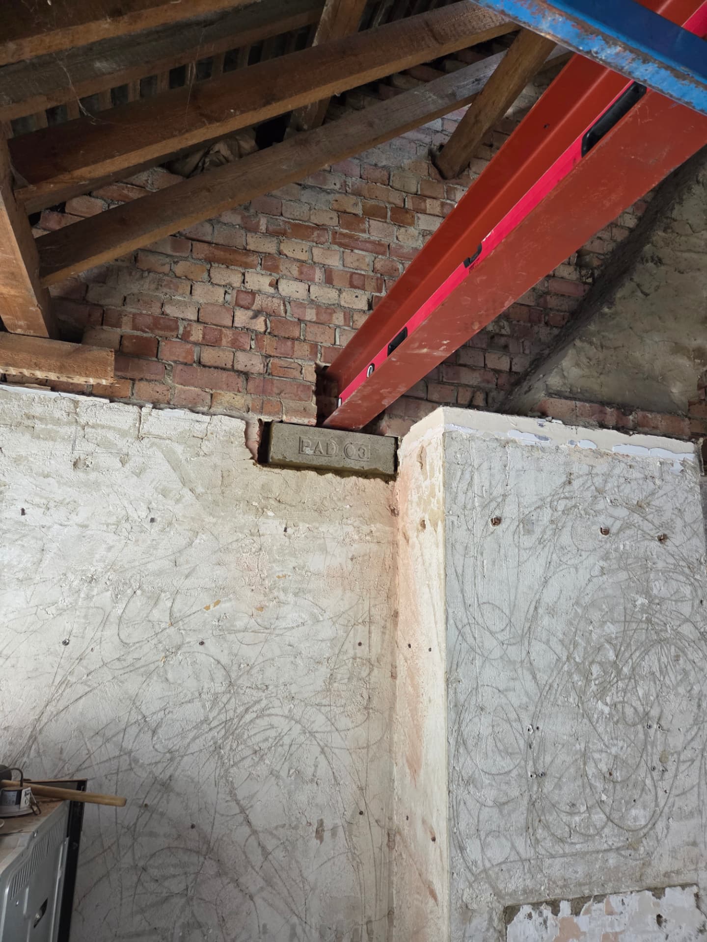 Red oxide steel beam seated into a brick wall above a concrete padstone during a loft conversion